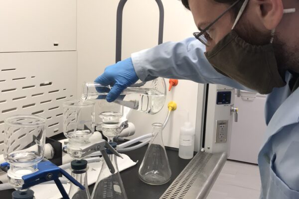 a man wearing gloves and a lab coat looking at a microscope