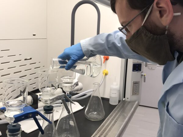 a man wearing gloves and a lab coat looking at a microscope